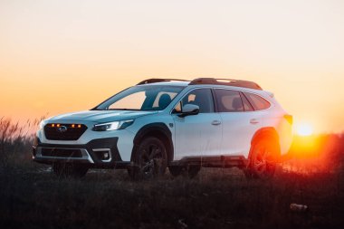 Brno, Çek Cumhuriyeti - 10 Şubat 2026: Subaru Outback 2.5 in white. Japon cipi kışın gün batımında bir çayırda. Aile büyüklüğünde bir araba, doğa gezisinde..