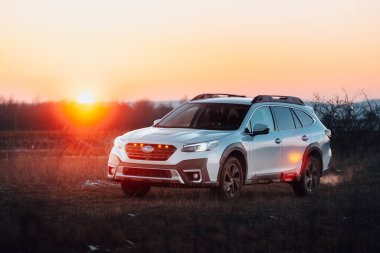 Brno, Çek Cumhuriyeti - 10 Şubat 2026: Subaru Outback 2.5 in white. Japon cipi kışın gün batımında bir çayırda. Aile büyüklüğünde bir araba, doğa gezisinde..