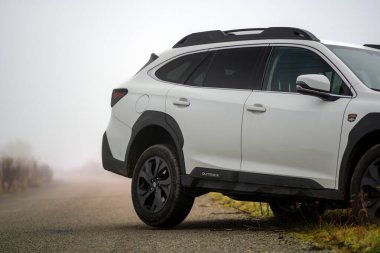Brno, Çek Cumhuriyeti - 12 Kasım 2025: Beyaz Subaru Outback aile arabası sonbaharda bir arazide siste duruyor. Off-road SUV arka tekerlek detayı.