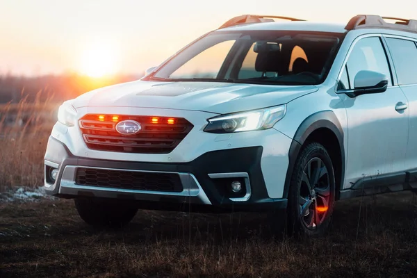 Brno, Çek Cumhuriyeti - 10 Şubat 2026: Japon SUV Subaru Outback 2.5 beyaz renkli bir arazi aracı gün batımında bir çayırda duruyor. Arabanın ön ızgarasında turuncu ışıklar var..