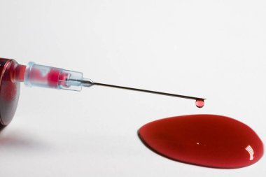 Beyaz arka planda bir damla kan olan hipodermik iğne.