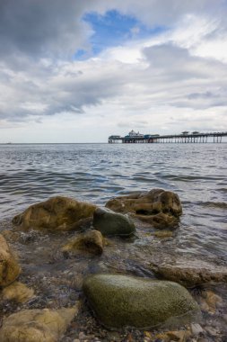 Rocky, Llandudno, Kuzey Galler 'deki engebeli kıyı şeridi. Islak kayalar ve kumsalda Llandudno iskelesi manzaralı düz bir deniz.