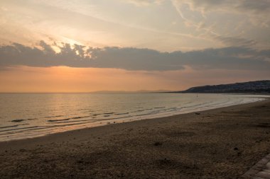Colwyn Körfezi, Kuzey Galler 'in yukarısında dramatik bir gökyüzü. Sakin bir denizle sahilde şafak sökerken