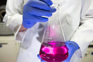 Laboratuvarda bir bilim adamı mor bir kimyasalın bulunduğu hacimli bir matarayı tutuyor. Başlık analizi