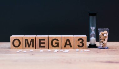 Omega 3, tahta küplerin üzerindeki kelime, tahta ve gri arka planda, küp haplarının ve kum saatinin yanında duruyor. Tıbbi ve sağlık hizmetleri kavramı