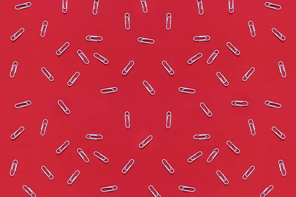 White paper clips are scattered on a red background. Top view, flat lay. Back to school, college, education concept. Abstract background