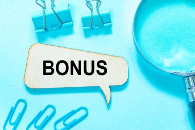 Ataç ve raptiyeli açık mavi arka planda bonus sözcüğüyle tahta top, büyüteç. Finans ve ekonomi kavramı.