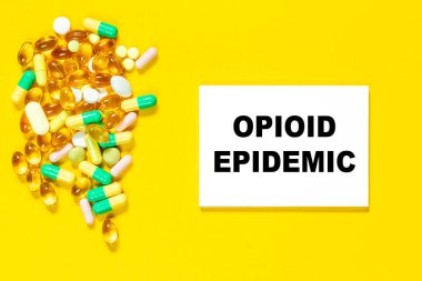 OPIOID EPIDEMIC kelimesi sarı arkaplanda renkli haplarla birlikte yapılmış. Tıbbi konsept.