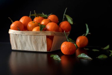 Fresh tangerine lies on a black table in the background there is a basket with tangerines.