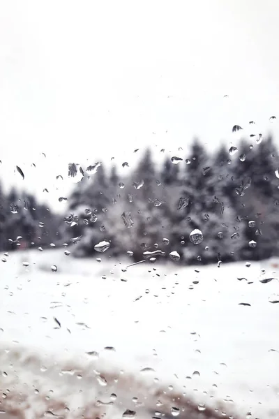 Raindrops on the window pane. Outside the window is a blurred landscape of a forest covered with snow. Winter. Background.