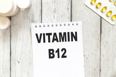 B-12 vitamini, kapsüllerin ve tabletlerin yakınındaki tahta masa arkaplanı üzerinde beyaz not defteri kağıdı üzerinde metin
