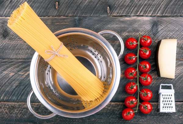 Spaghetti pasta, tomatoes, cheese, colander and grater on old ru — Stock Photo, Image