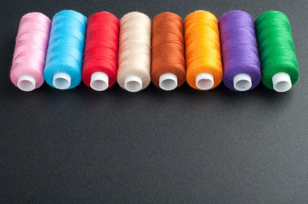 Spoelen met verschillende kleuren van draad op donkere achtergrond. Naaien — Stockfoto