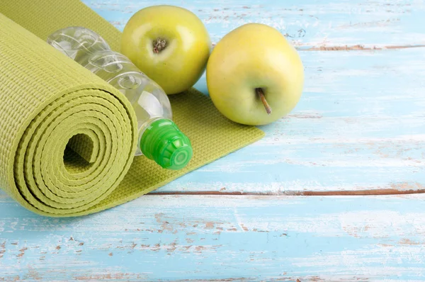 Tapis de yoga, bouteille d'eau et pommes sur un fond en bois. Éq. — Photo
