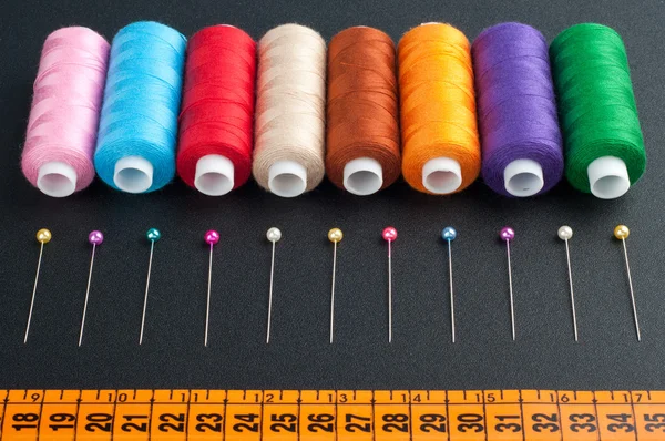 Spools with various colors of thread and pins on dark background — Stock Photo, Image