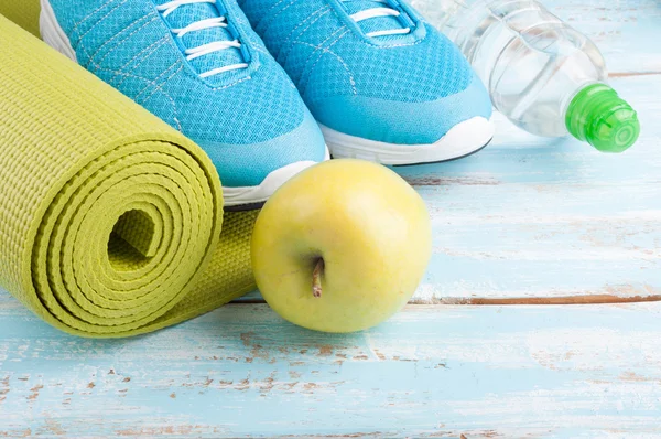 Tapis de yoga, chaussures de sport, pomme, bouteille d'eau sur bac en bois bleu — Photo