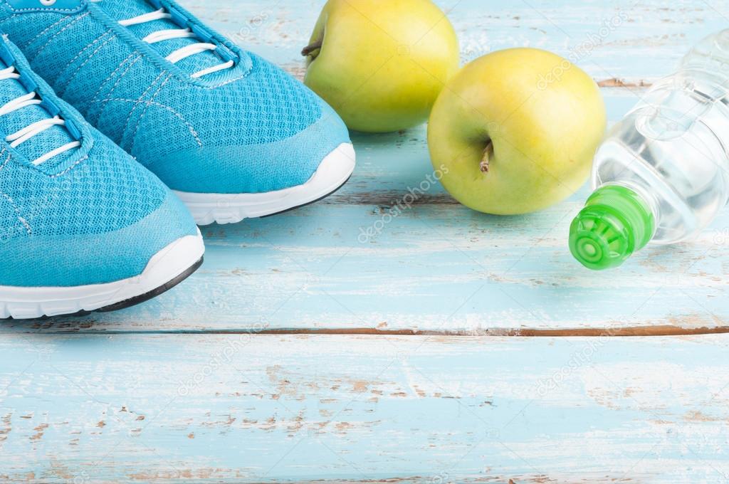 Sport shoes, apples, bottle of water on blue wooden background. 