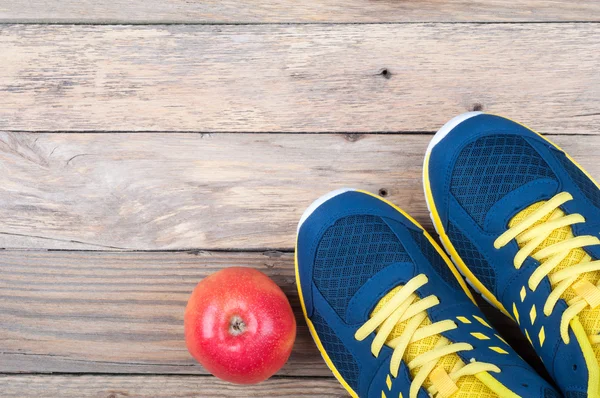 Sport cipők és alma a fából készült háttér. Sportfelszerelés. Egészséges életmód — Stock Fotó