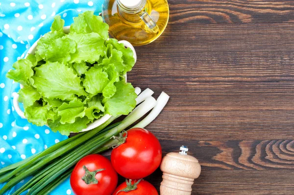 Healthy food concept background with copy space. Organic vegetables - lettuce, green onions, tomatoes and olive oil, salt on wooden table. Cooking salad
