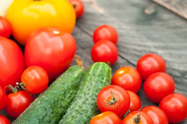 Grönsaker bakgrund. Tomater och gurkor på träbord — Stockfoto