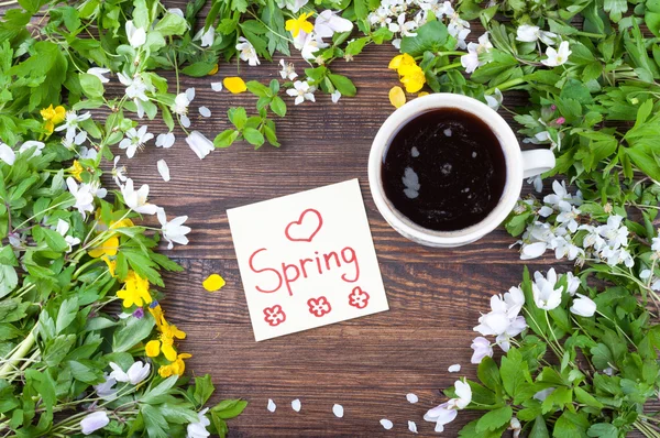 Kopje koffie op de achtergrond van de lente. Koffie, bloemen, opmerking met woord lente op een houten ondergrond — Stockfoto