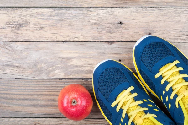 Zapatillas deportivas y manzana sobre fondo de madera. Equipamiento deportivo — Foto de Stock