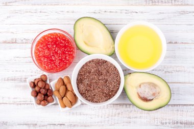 Foods with healthy fats. Sources of omega 3 - avocado, olive oil, red caviar, nuts and flax seed on wooden background. Healthy food concept clipart