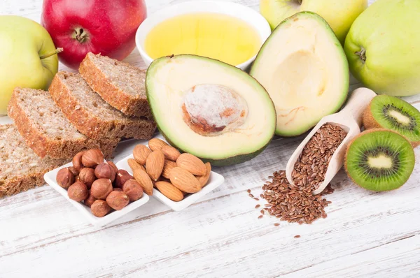 Gesunde Fettquellen und gesunde Nahrung - Avocado, Leinsamen, Olivenöl, Vollkornbrot, Nüsse, Kiwi und Äpfel auf Holzuntergrund mit Kopierfläche. — Stockfoto