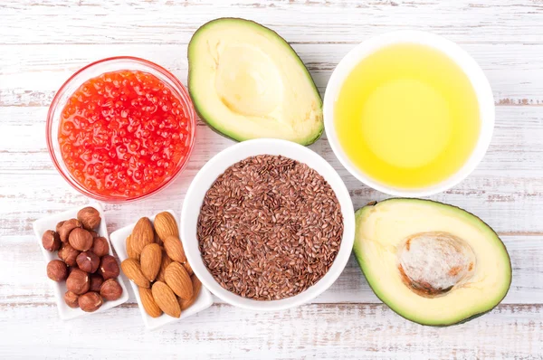 Hälsosamma fetter. Källor till omega 3 - avocado, olivolja, röd kaviar, nötter och linfrö på trä bakgrund. Hälsosam mat koncept Stockfoto