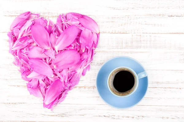 Filiżankę kawy i piwonie płatki w kształcie serca na tle rustykalne drewniane. Letnie kwiaty — Zdjęcie stockowe
