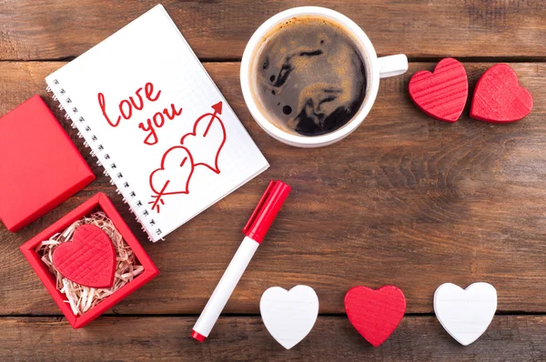 Romántico Te amo nota en bloc de notas, taza de café y corazones decorativos sobre fondo de madera vieja. Fondo día de San Valentín — Foto de Stock