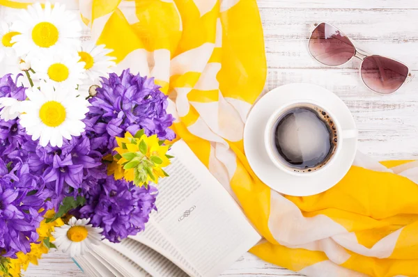 Tazza di caffè, libro, mazzo di fiori, accessori donna occhiali da sole e fazzoletto su sfondo di legno. Estate riposo concetto di sfondo — Foto Stock