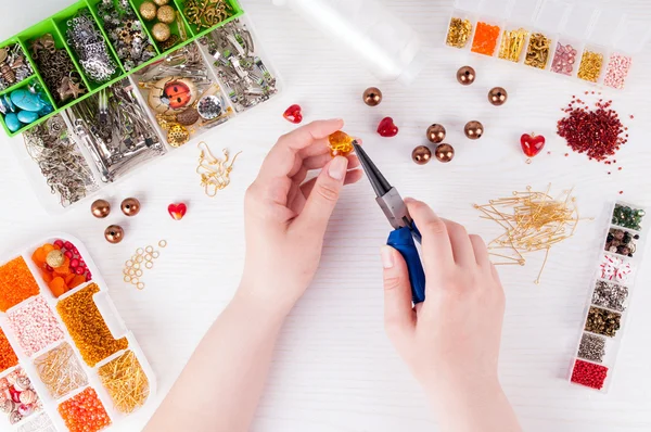 Frau stellt handgefertigten Schmuck her. Schachteln mit Perlen, Glasherzen, Zubehör für Handarbeiten auf weißem Holztisch. Handgemachtes Zubehör — Stockfoto