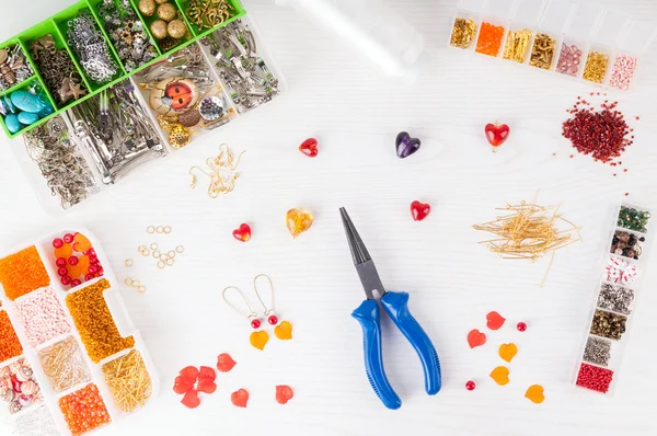 Herstellung von handgefertigtem Schmuck. Schachteln mit Perlen, Zangen, Fäden, Ausrüstung und Zubehör für die Handarbeit auf einem Holztisch. Prozess der Handarbeit — Stockfoto