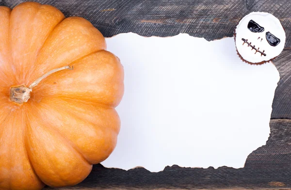 Halloween Hintergrund mit altem Papier für Ihren Text. Kürbis-Muffin mit Totenkopf für Halloween-Party auf altem rustikalen Holztisch — Stockfoto