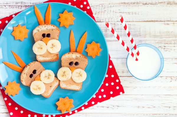 Café da manhã infantil com sanduíches e leite. Sanduíches engraçados de cara de coelho com manteiga de amendoim, banana e cenoura — Fotografia de Stock