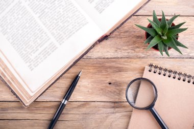 Açık kitap, etli, kalem, defter ve Büyüteç rustik ahşap zemin üzerinde. Ofis resepsiyon masası. Üstten Görünüm