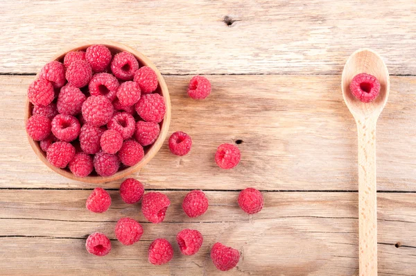 Fresh ripe raspberries in a bowl and spoon with berry on old wooden table — Stock Photo, Image