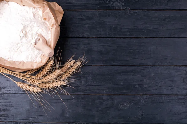 Baking background. Flour in paper bag and wheat on dark wooden table. Ingredients for cooking — Stock Photo, Image