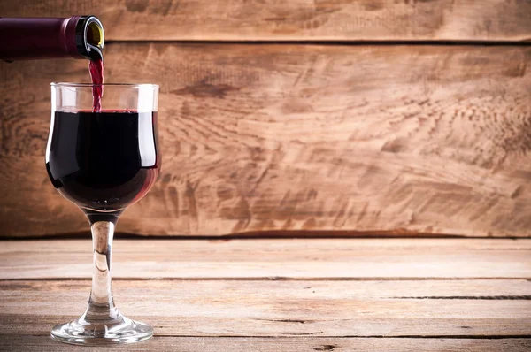 Red wine. Pouring red wine into wine glass on old rustic wooden boards. Wine background — Stock Photo, Image