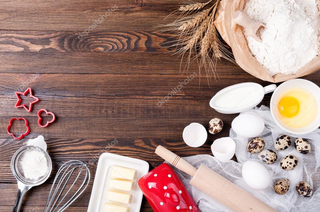 Ingredients for baking. Flour in paper bag, eggs, butter, milk, rolling pin, whisk and cookie cutters on wooden background. Cooking cookies