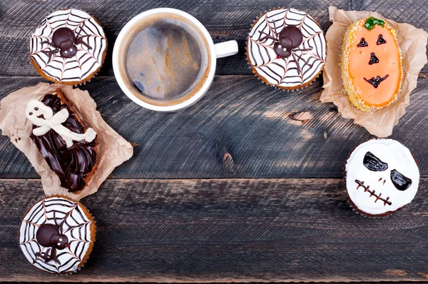Halloween background. Funny pumpkin muffins with spiders, scull, ghost and cup of coffee for halloween party on old rustic wooden table. Copy space