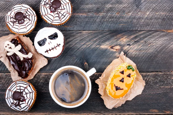 Halloween background. Funny pumpkin muffins with spiders, scull, ghost and cup of coffee for halloween party on old rustic wooden table