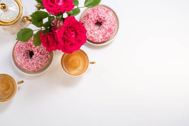 Çöreklerle kahvaltı, kahve fincanı ve çiçeklerle beyaz şarap arkaplanındaki pembe gül kompozisyonu. Düz konum, üst görünüm, kopyalama alanı
