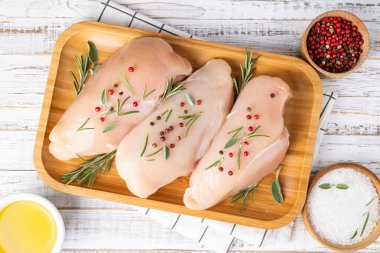 Çiğ tavuk göğsü. Baharatlı ve otlu beyaz ahşap arka plan. Pişirmek için malzemeli et. Üst görünüm