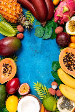 Taze tropikal meyve düzlüğü. Mavi yaz tropik arka planında farklı egzotik meyveler. Taze meyve arka planı. Seyahat ve tatil. Sağlıklı yemek, diyet, vegan, vejetaryen konsepti. Boşluğu kopyala
