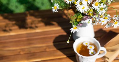 Tahta kırsal masada bir fincan papatya çayı. Papatyalı bitki çayı, bir buket çiçek ve not defteri. Alternatif, bitkisel ilaçlar, eczane konsepti. Boşluğu kopyala