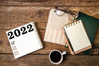 Yeni Yıl Kararları 2022 listesi. Not defterleri, kahve fincanı, Amerikan bayrağı olan ofis masası. Hedef, plan, fikirler, iş, motivasyon, kontrol listesi kavramı