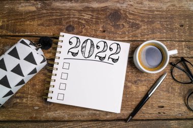 Yeni yıl hedefleri 2022 masada. Ahşap arka planda defter, kahve fincanı ve gözlüklü 2022 karar listesi. Hedefler, plan, strateji, iş, fikir, eylem konsepti