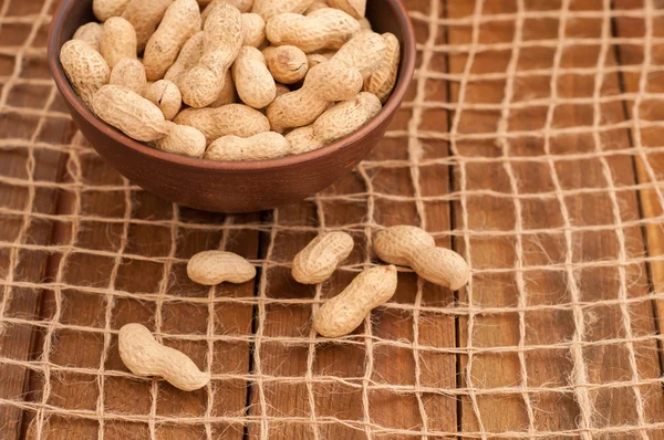 Peanuts in a bowl on a grid of twine. Wooden brown background — Stock Photo, Image